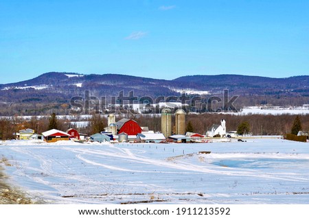 Winter scene with farm buildings, field and hills, upstate New York. Farmhouse, red barn, silos or grain bins