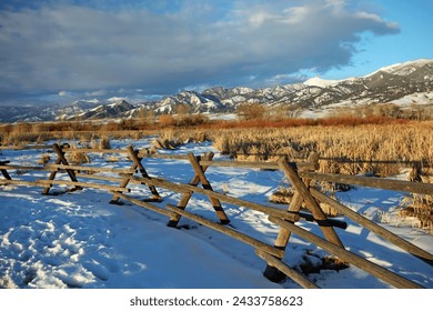 Winter scene in Montana with wooden criss cross fence, snow and mountains