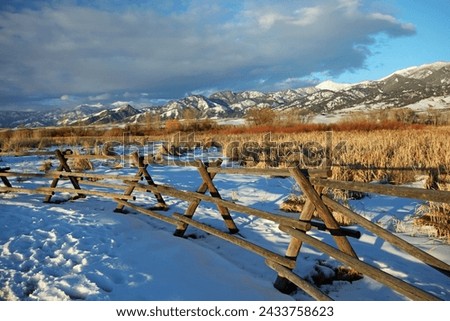 Winter scene in Montana with wooden criss cross fence, snow and mountains