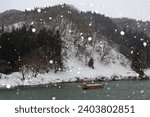 Winter scene of a sightseeing boat cruising in snowfall on Mogami-Gawa, which is regarded as one of the three most rapid rivers in Japan, with riverside mountains covered by heavy snow