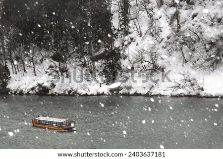 Winter scene of a sightseeing boat cruising in snowfall on Mogami-Gawa, which is regarded as one of the three most rapid rivers in Japan, with riverside mountains covered by snow