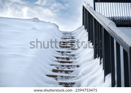 Winter scene where a set of stairs is almost completely covered in snow and railing on the right side of the stairs