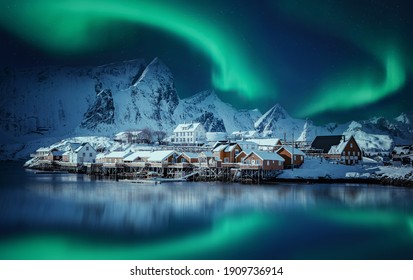 Winter scenery with aurora over Reine. Incredible winter view on snowcapped mountains, fishing village and Northern lights. Typical nature landscape of Lofoten islands. Norway. creative poscard 