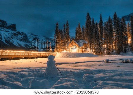 Winter scenery of Emerald lake with wooden lodge glowing in pine forest and snowman in the night on winter at Alberta, Canada
