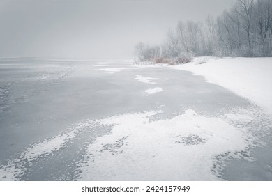 Winter scenery with a frozen lake and snowy shore. Trees and reeds with the rime on a coast. Winter foggy landscape. - Powered by Shutterstock