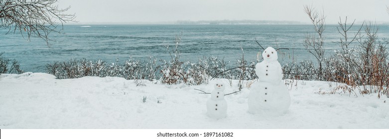 Winter Scenery Fun Outdoor Activity For Kids, Building Snowman In Snow In Quebec, Canada. Nature Fun Banner. Two Snowmen In Front Of Water.