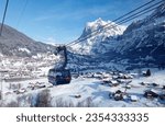 Winter scenery of Grindelwald village on the snowy hillside with Wetterhorn mountain under blue sky in background, viewed from a gondola of Eiger Express cableway, in Berner Oberland, Switzerland