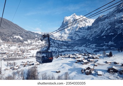 Winter scenery of Grindelwald village on the snowy hillside with Wetterhorn mountain under blue sky in background, viewed from a gondola of Eiger Express cableway, in Berner Oberland, Switzerland