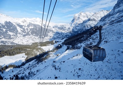 Winter scenery of Grindelwald village in the snowy valley with Wetterhorn mountain under blue sky in background, viewed from a gondola of Eiger Express cableway, in Berner Oberland, Switzerland - Shutterstock ID 2358419639