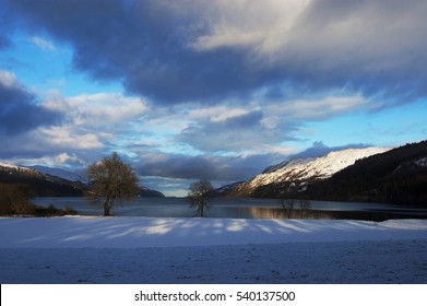 Winter scenery on the banks of Loch Ness lake with trees and snowy mountains