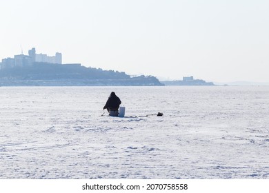 Winter Sea Fishing In Vladivostok. A Fisherman Is Fishing Across The Frozen Sea.