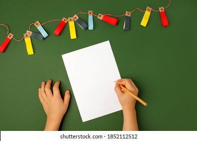 Winter Season Holiday, Christmas, New Year. Xmas Concept. Children's Hands Writing On Empty Card Mock-up. Flat Lay Top View, Natural Shades Of Green. Learning To Draw, Making Wish List Or Plans