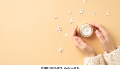 Winter season skin care cosmetics concept. First person top view photo of woman's hands in knitted sweater small cream jar and snowflakes on isolated pastel beige background with empty space - Shutterstock ID 2227173543