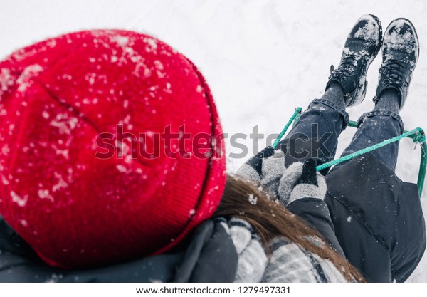 Winter season, snowing outside.
Riding the sledge concept. The woman in red hat is sitting on the
sled. Hands in gloves with a green sled rope. Top view
photo.