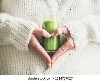 Winter seasonal smoothie drink detox. Female in woolen sweater holding bottle of green smoothie or juice making heart shape with her hands. Clean eating, weight loss, healthy dieting food concept