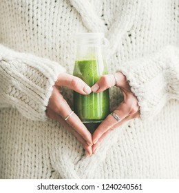 Winter seasonal smoothie drink detox. Female in sweater holding bottle of green smoothie or juice making heart shape with her hands, square crop. Clean eating, weight loss, healthy dieting food