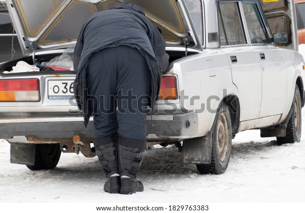 Winter sketch. A man in\
warm clothes leaned over the open trunk of an old rusty car. He\'s\
going fishing.