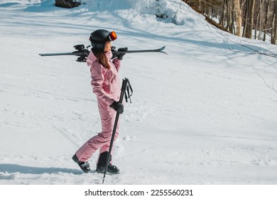 Winter Skiing. Ski portrait of woman alpine skier holdings skis wearing helmet, cool ski goggles, hardshell winter jacket and ski gloves on snow covered ski trail slope