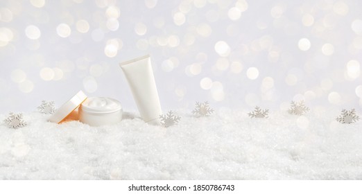 Winter Skin Care Cosmetic Products In Snow And Snowflakes On White Background With Bokeh Lights. Opened Face Cream Jar And Hand Creme Or Body Lotion Tube. Festive Banner With Copy Space For Text