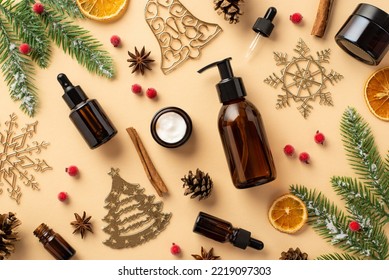 Winter skincare cosmetics concept. Top view photo of pump bottle dropper bottle cream jar christmas ornaments mistletoe fir branches pine cone cinnamon dried orange slices on isolated beige background