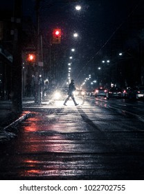 Winter Snow Storm With Man Crossing Street. Silhouetted Figure Walking Across Downtown, Urban, City Street In Heavy Snowfall And Traffic. Canadian Winter Night Scene. Toronto, Ontario, Canada