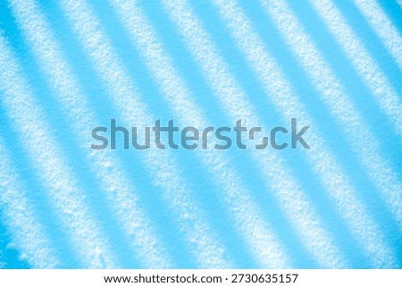 Winter snow surface showing intriguing abstract patterns of diagonal shadow stripes, creating a cool blue and white texture background for seasonal or conceptual designs
