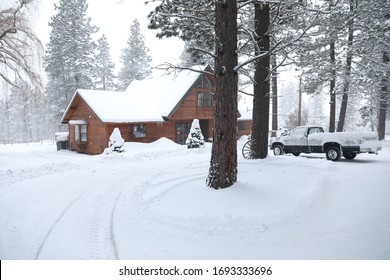 WInter Snowy Cabin House Exterior With Forest And Pine Trees And Snow Mobile Tracks.