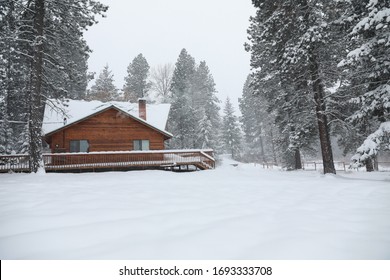 WInter Snowy Cabin House Exterior With Forest And Pine Trees And Snow Mobile Tracks.