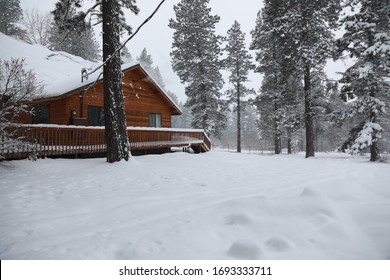 WInter Snowy Cabin House Exterior With Forest And Pine Trees And Snow Mobile Tracks.