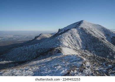 Winter snowy panorama of neighboring mountains and hills from Mount Beshtau with snow-covered and icy grass, sunny winter day