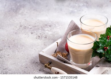 Winter spicy hot drink eggnog in a glasses with cinamon in stone plate, ice frost branches on light stone table