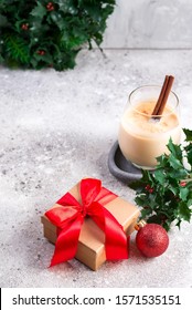Winter spicy hot drink eggnog in a glass with cinamon and gift box on light stone table