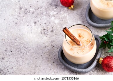 Winter spicy hot drink eggnog in a glasses with cinamon in stone plate, ice frost branches on light stone table