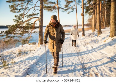 Winter Sport In Finland - Nordic Walking. Man And Senior Woman Hiking In Cold Forest. Active People Outdoors. Scenic Peaceful Finnish Landscape With Snow.