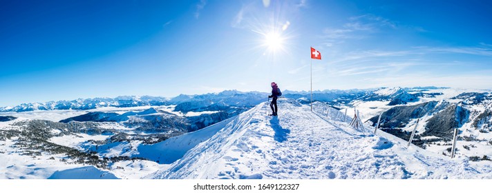 winter sports: snow shoe hiker a the top of the snowy mountain in the swiss alps. panoramic picture of winter hiker at the top of the hill in switzerland. mountain panorama with sun and blue sky
