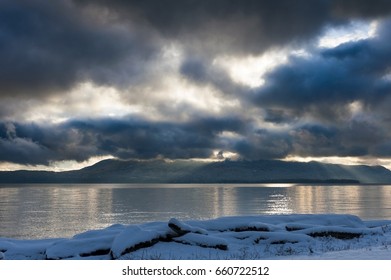 A Winter Storm In The San Juan Islands. Snow Covers The Coastline On Lummi Island In The San Juan Island Archipelago. Dramatic Clouds Cover The Sky All The Way To The Horizon.