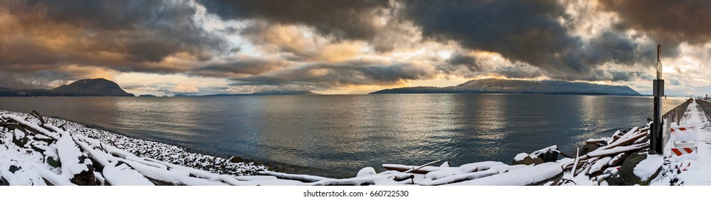 A Winter Storm In The San Juan Islands. Snow Covers The Coastline On Lummi Island In The San Juan Island Archipelago. Dramatic Clouds Cover The Sky All The Way To The Horizon.