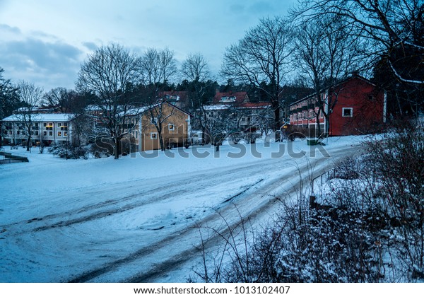 Winter street with car\
marks left on the recently fallen snow in Stockholm suburb Bromma.\
The background has some typical Swedish apartment buildings in\
beautiful colors.
