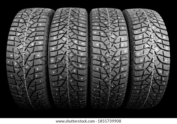 Winter studded tire. Winter car tires isolated on\
black background. Tire stack background. Tyre protector close up.\
Square powerful spikes. Black studdable winter tyre profile. Car\
tires in a row