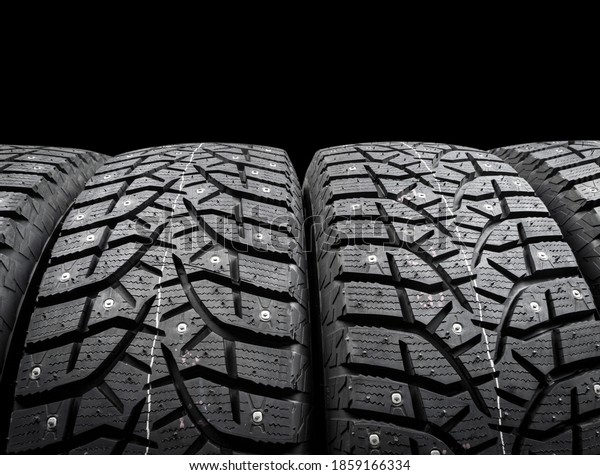 Winter studded tire. Winter car tires isolated on
black background. Tire stack background. Tyre protector close up.
Square powerful spikes. Black studdable winter tyre profile. Car
tires in a row