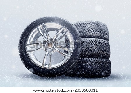 winter studded tires, a set of friction winter wheels with aluminum alloy wheels on a white background. falling snow is a safety concept about seasonal tire change for safety on the road in icy