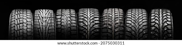 a lot of winter studded tires\
and velcro tires stand in a row on a black background\
panorama