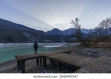 Winter sunset behind a mountain peak of a winter alpine landscape with hiker on wooden pier at reservoir lake at Barcis, Friuli-Venezia Giulia, Italy - Powered by Shutterstock