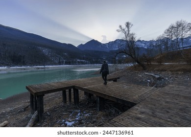 Winter sunset behind a mountain peak of a winter alpine landscape with hiker on wooden pier at reservoir lake at Barcis, Friuli-Venezia Giulia, Italy - Powered by Shutterstock