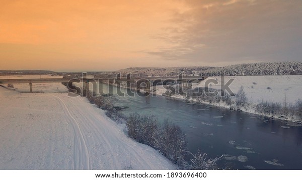 Winter. Sunset. bridge across Dnieper. Belarus.\
Aerial photos from drone of river against the background of forest\
and bridge, cars moving along it. Rural area. The sunset or\
sunrise, beautiful sun.