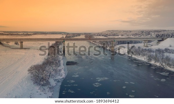 Winter. Sunset. bridge across Dnieper. Belarus.\
Aerial photos from drone of river against the background of forest\
and bridge, cars moving along it. Rural area. The sunset or\
sunrise, beautiful sun.