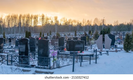 Winter sunset over a snow covered cemetery with dark headstones and trees. Afterlife. Samsara concepts. Hope for the resurrection of the dead. Space for text.