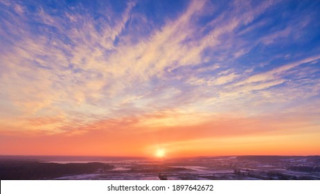 Winter sunset rural Skyscape - Stunning epic sunset sky with the setting sun on the horizon. Pink-orange winter frosty sunset against a bright blue sky with Spindrift clouds.