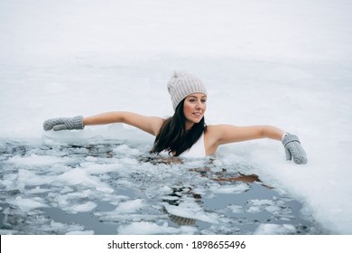 Winter Swimming. Woman In Frozen Lake Ice Hole. Swimmers Wellness In Icy Water. How To Swim In Cold Water. Beautiful Young Female Smiling. Gray Hat And Gloves Swimming Clothes. Nature Lake In Forest