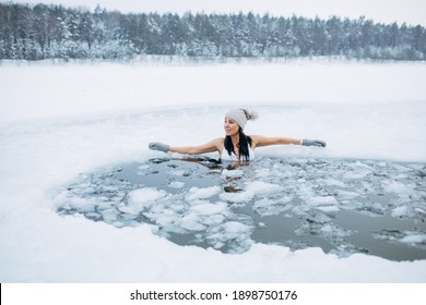 Winter Swimming. Woman In Frozen Lake Ice Hole. Swimmers Wellness In Icy Water. How To Swim In Cold Water. Beautiful Young Female Smiling. Gray Hat And Gloves Swimming Clothes. Nature Lake In Forest